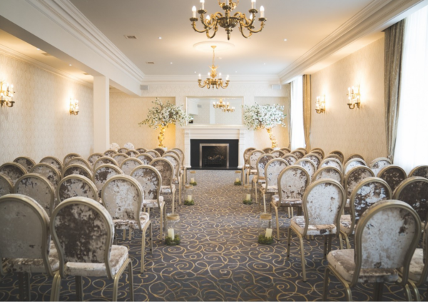 A light coloured room set up for a wedding with white flowers and white chairs
